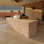 beige stone outdoor kitchen with steel grill on outdoor patio