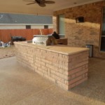 beige stone outdoor kitchen with steel grill on outdoor patio