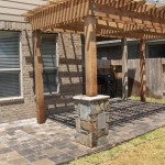 wooden pergola with stone posts next to beige home and wooden fence