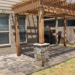 wooden pergola with stone posts next to beige home and wooden fence